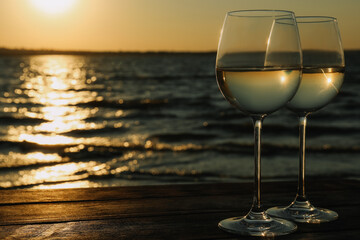 Two glasses of wine on wooden table near river at sunset. Space for text