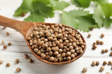 Spoon with dried coriander seeds and green leaves on wooden table, closeup