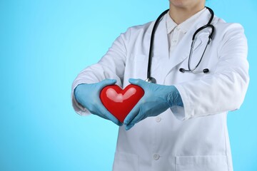 Doctor with red heart on light blue background, closeup. Space for text