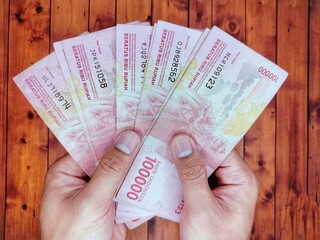 Man's hand holding one hundred thousand rupiah bill One hundred thousand in hand stacked like a fan