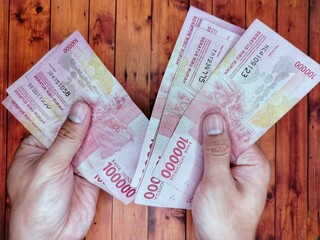 Man's hand holding one hundred thousand rupiah bill One hundred thousand in hand stacked like a fan