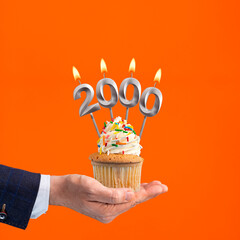 Hand holding birthday cupcake with number 2000 candle - background orange