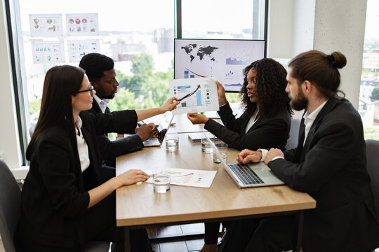 Diverse business team engaged in discussion with charts and graphs during meeting in modern office. Professionals collaborating, analyzing data, and strategizing for business growth.