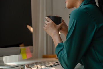 a businesswoman is in the conference meeting, a head of marketing department is listening her team present new marketing strategy plan via computer and holding a cup of coffee