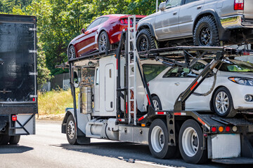 Long car hauler big rig semi-truck transporting cars on the hydraulic semi trailer driving on the...