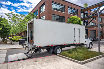 Middle duty day cab moving rig semi truck with long box trailer and lift on the back standing on...