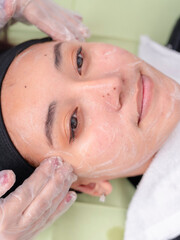 A woman enjoys a relaxing facial massage with cream at a beauty spa, preparing for facial or vacuum suction or other treatment.