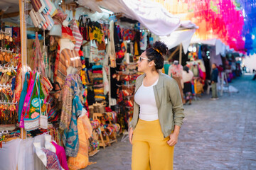 Young Latina woman browsing market stalls filled with colorful goods. Curious and engaged. Taken in the historic center of Oaxaca, Mexico.