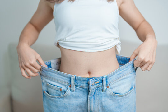 young slim female wearing big or oversize jeans, woman show healthy shape after weight loss. dieting, exercise, body fit and liposuction surgery concept