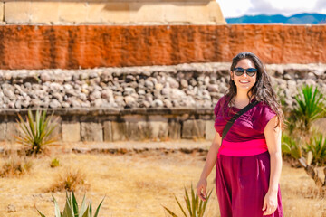 Fototapeta premium Young Latina woman smiling at Mitla ruins, Oaxaca, Mexico, wearing traditional dress and sunglasses on a sunny day.