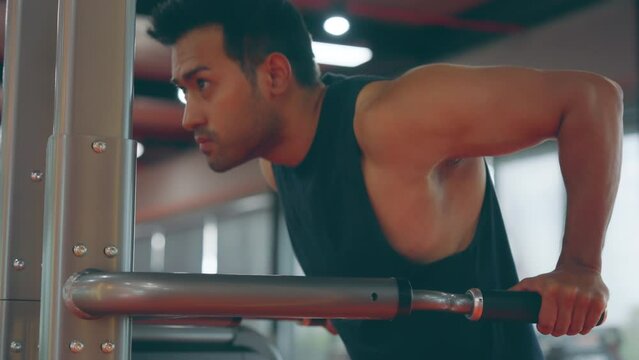 Motivated young asian sportsman having workout on machine. Handsome man bodybuilder training body on modern exercises in gym