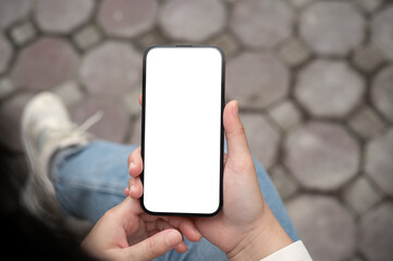 A woman holding a smartphone with a white-screen mockup over her lap while sitting outdoors.