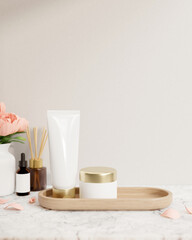 A lotion tube and a facial cream jar mockup are on a white marble tabletop against the white wall.