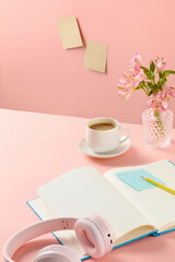 Top-down shot of a pink desk with some essential working items, a morning milk coffee cup and a decorative flower vase placed in a corner. Space on table for showing product