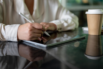 A cropped image of a businesswoman holding a stylus pen, writing on her digital tablet.