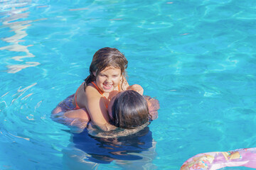 a mother holds her beautiful daughter in her arms teaching her to swim in the pool