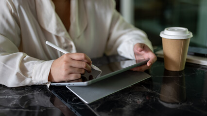A cropped image of a businesswoman holding a stylus pen, writing on her digital tablet.
