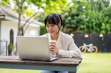 A businesswoman sipping coffee while focusing on reading emails on her laptop computer in a garden.