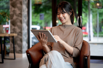 A pretty, positive young Asian woman using her digital tablet in a coffee shop.