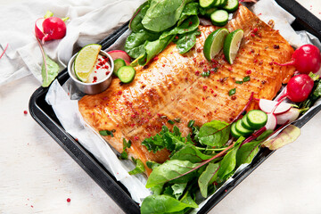 Cooked salmon with fresh greens and lime. Baked redfish on light wooden background