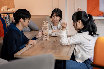 A group of happy, fun Asian friends is enjoying playing Jenga game together at home.