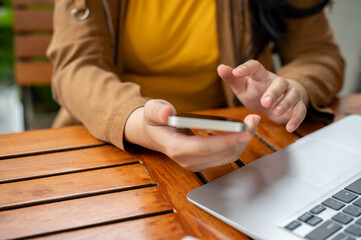 A cropped image of a woman using her smartphone at a table while working remotely from a cafe.