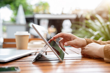 A side view image of a woman touching on a digital tablet screen, working remotely on her tablet.