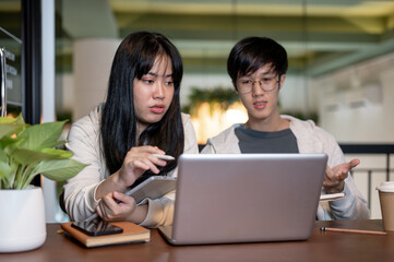 Two young Asian college student friends are working on a co-project together at a cafe.