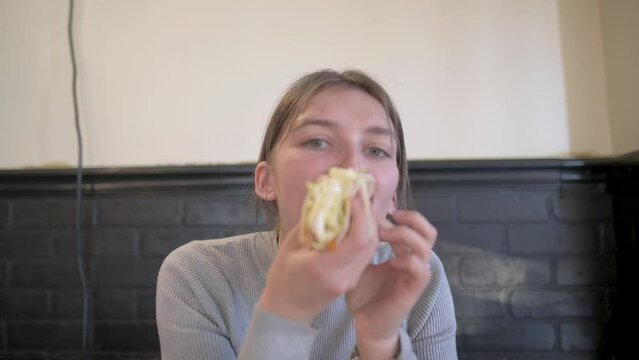 A woman in a casual restaurant setting, holding and eating a taco, enjoying a relaxed meal.