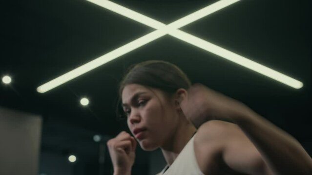 Close-up shot of face and hands of young muscular Hispanic female boxer shadowboxing alone in empty gym at night, working on punches, jabs and lunges