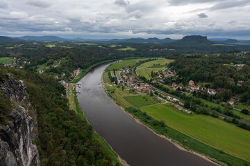 A river runs through a town with houses and trees in the background. The water is brown and the sky is cloudy