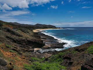 Scenic view of a rocky coastline and sandy beach with clear blue ocean in Oahu