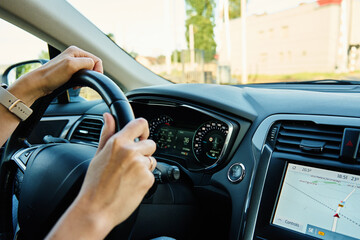 Close up view of female driver hands on steering wheel. Woman driving car at sunset. Inside view of modern vehicle moving on road