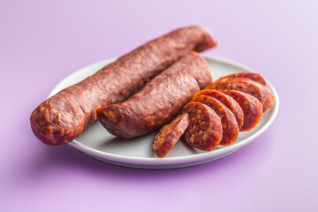 Sliced smoked salami sausage on plate on violet background.