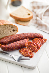 Sliced smoked salami sausage on wooden cutting board on white table.