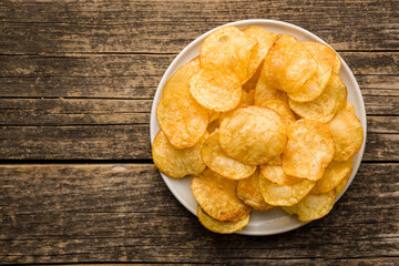 Crispy Potato Chips on plate on wooden table. Top view.