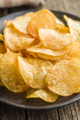 Crispy Potato Chips on plate on wooden table.