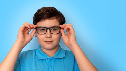 Close up of dark haired boy in glasses on light-blue background, look at camera