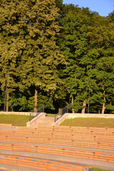 Siedzenia amfiteatru na zewnątrz na powietrzu w parku z drzewami w tle © VILKTERIO