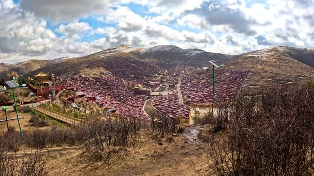 Panoramic static establishing view from mountains looking down on Larung Gar Tibetan Buddhist academy on sunny day