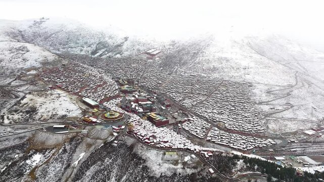 Aerial establishing overview of Larung Gar Tibetan Buddhist academy and town covered in snow, TIbet, China