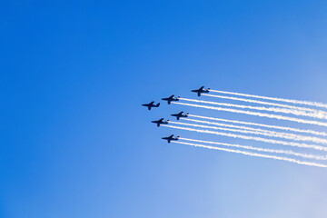 Fighter planes in formation flight with white condensation trails on a blue sky