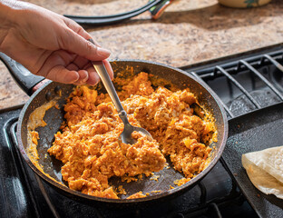 Concept of taking or grabbing food with hands, feminine Mexican hands. scrambled eggs with chorizo ​​in a skillet for Mexican breakfast horizontal
