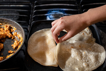 Concept of taking or grabbing food with hands, feminine Mexican hands. flour tortillas on comal to prepare breakfast and quesadillas, very Mexican breakfast horizontal