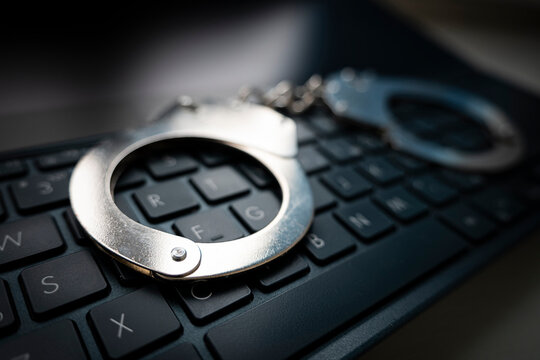 metal handcuffs on a black keyboard. Selective focus on handcuffs on a keyboard cyber crime, hacking, bullying Against law concept in dark low key tone
