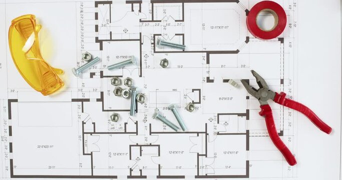 Worker hand pours bolts and nuts onto floor plan with tools view from above. Builder scatters fastening supplies onto printout drawing in office