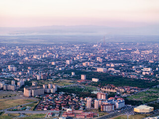 Aerial view of a vivid sunset over the city near hills. Panorama of streets and buildings. Vibrant color cityscape.