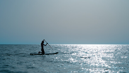 silhouette of person doing sup surfing on the sunset in the blue sea
