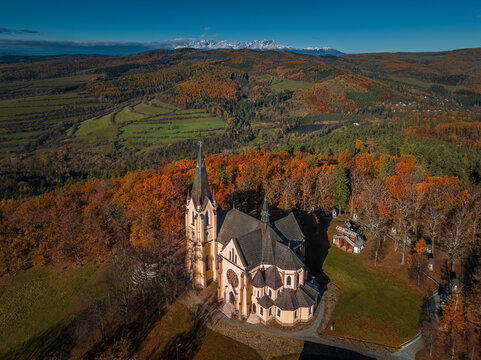 Levoca, Slovakia - Aerial view of Basilica of the Visitation of the Blessed Virgin Mary on a sunny autumn day with colorful autumn foliage. High Tatras mountains and clear blue sky at background