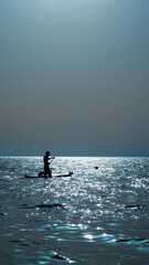 silhouette of person doing sup surfing on the sunset in the blue sea